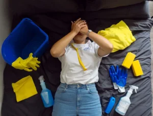 een vrouw met haar handen voor haar ogen en rondom haar allemaal schoonmaak spullen